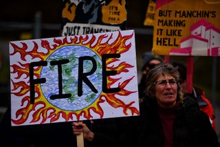 A climate activist holding a handmade sign with a drawing of the Earth on engulfed in flames and the words FIRE.