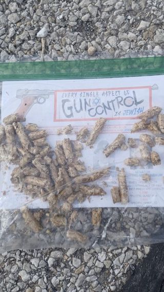 A flyer that reads “Every single aspect of gun control is Jewish” packed into a sandwich bag with rodent poison pellets sitting on cobblestone.