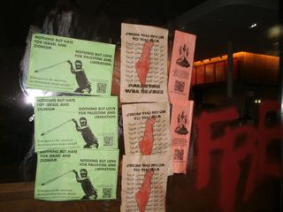 Closeup of posters wheatpasted on Starbucks window. They read, "NOTHING BUT HATE FOR ISRAEL AND ZIONISM, NOTHING BUT LOVE FOR PALESTINE AND LIBERATION" and "FROM THE RIVER TO THE SEA, PALESTINE WILL BE FREE."